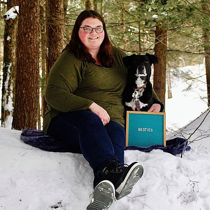 A woman and her dog sitting on snow, holding a sign titled "BESTIES".