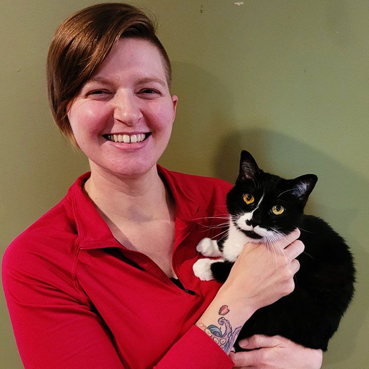 Woman in red shirt smiling and holding a black and white cat.