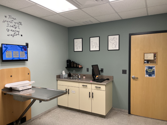 Interior of a veterinary clinic with cabinets, a desk, and animal art on the wall.