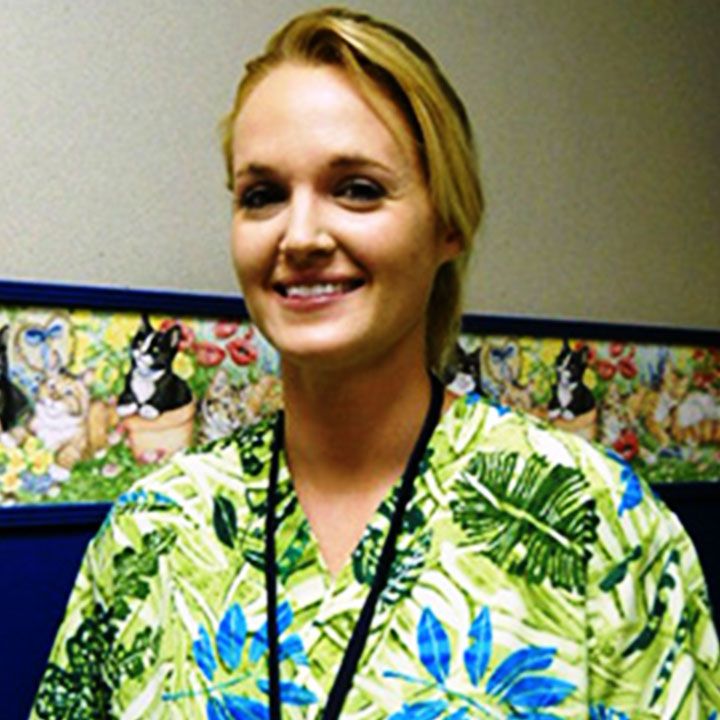 Smiling woman in a floral patterned shirt with a lanyard around her neck.