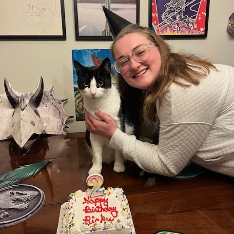 A woman and a black and white cat celebrating the cat's birthday with a cake.
