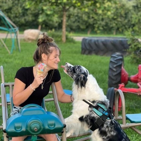 Woman laughs as a dog licks her face, sitting outdoors.