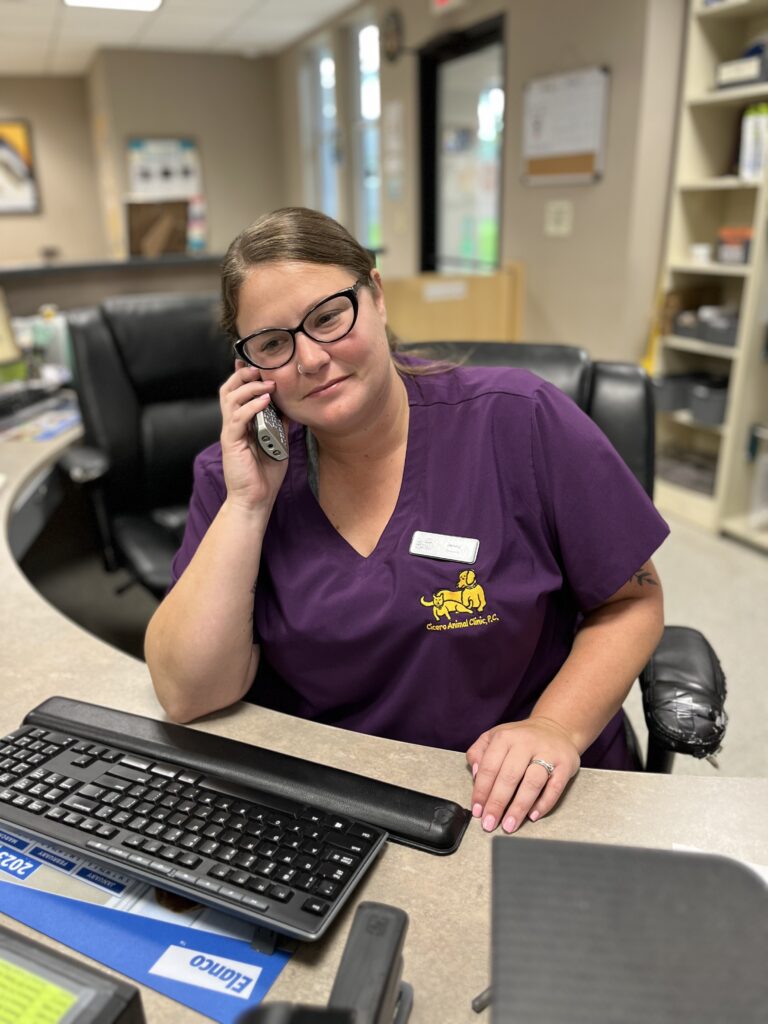 Woman in purple scrubs talking on a phone at a veterinary clinic reception desk.