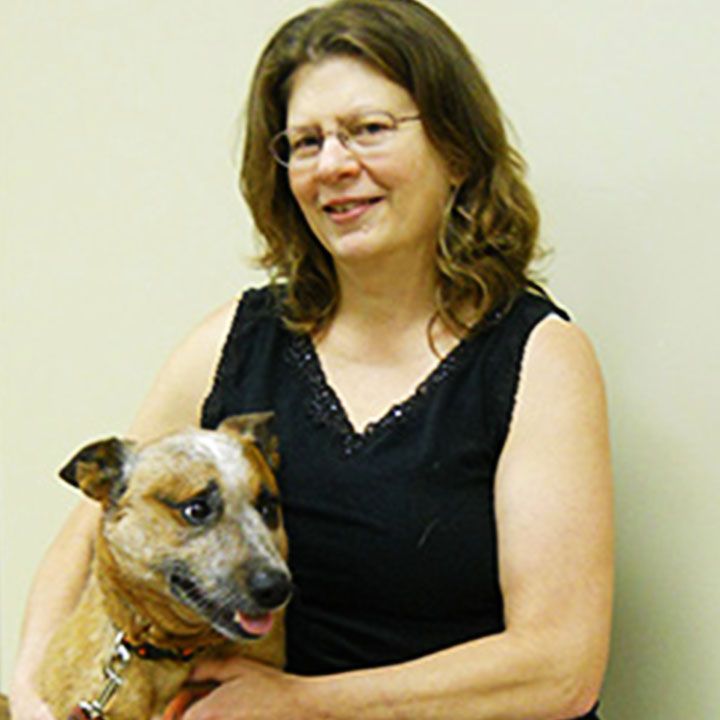 Woman in black sleeveless top smiling and holding a small, brown dog.