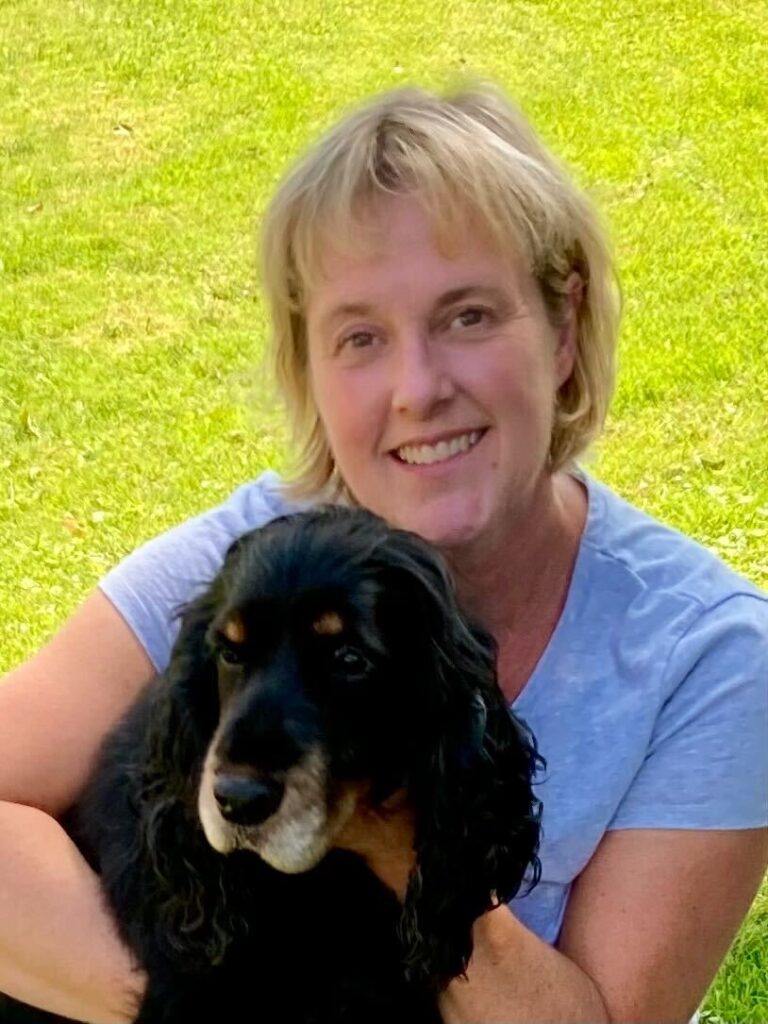 A smiling woman holding a black and brown dog on a grassy field.