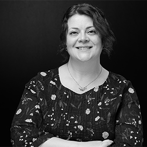 A monochrome portrait of a smiling woman with medium-length hair, wearing a floral blouse.