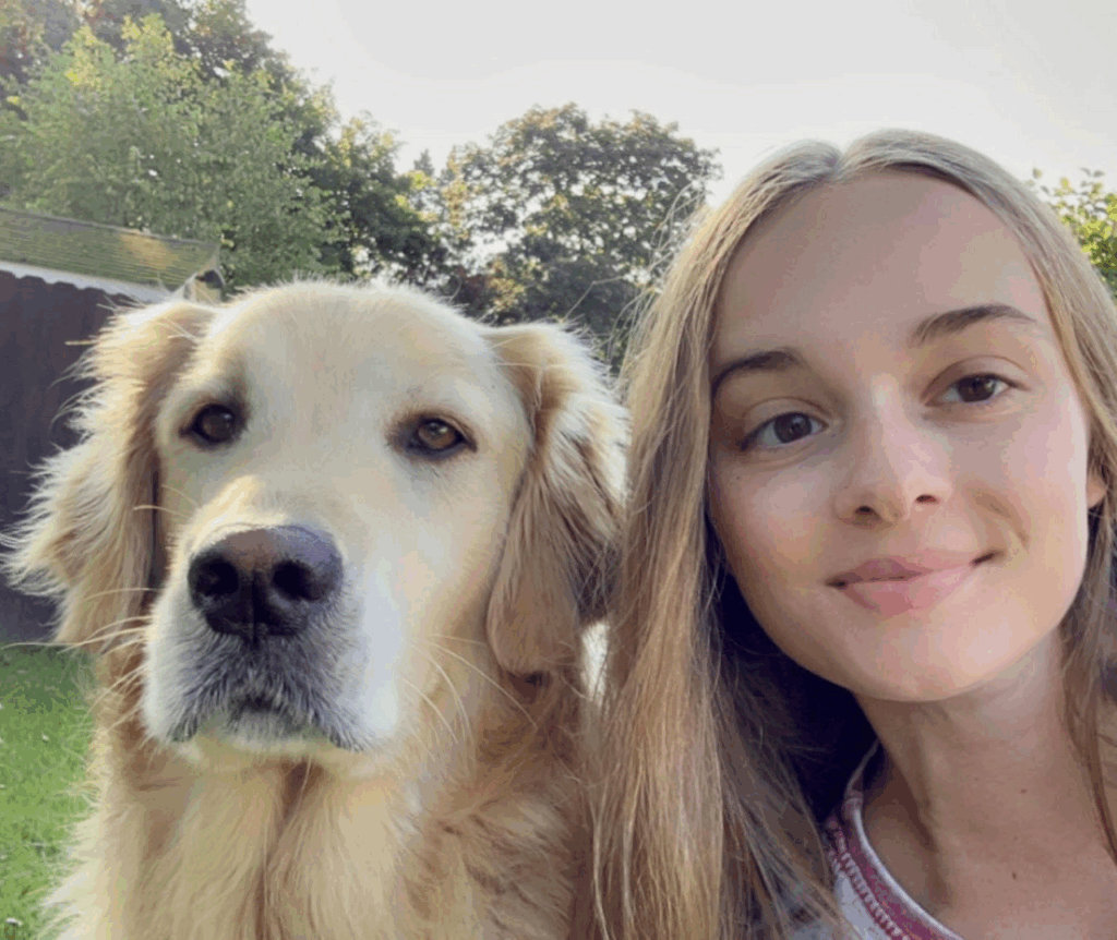 Young woman and a golden retriever posing together outdoors.